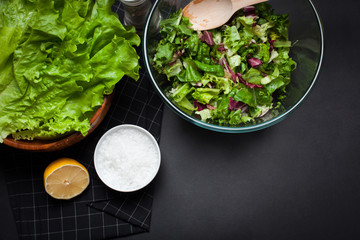 Fresh vegetarian salad mix in a clear glass bowl on a black background.