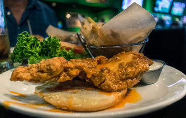 close up of delicious buffalo chicken sandwich on a plate with french fries, lettuce and tomato served at a sports bar