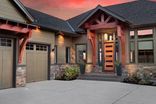 Beautiful Luxury Home Exterior at Sunset: Front Entrance with Elegant Front Door and Partial View of Garage and Driveway. Colorful Sunset Backdrop