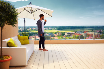 young adult man standing on rooftop terrace, enjoying beautiful cityscape view