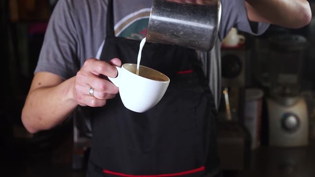 Video footage of a male barista prepares a cup of hot coffee with a cup of milk