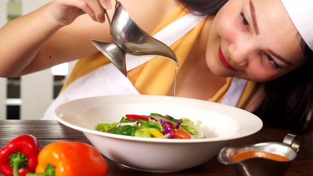 Video footage of a young female chef serving a plate of vegetable salad with olive oil in the restaurant