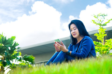 Asian woman chatting on mobile phone and smiling at screen sitting on grass outside home