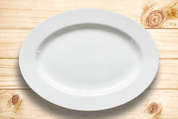 Top view of empty white food plate on a wood background.