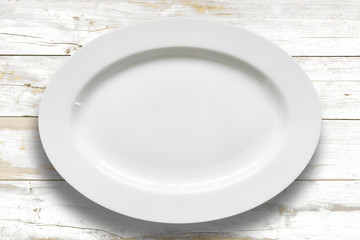 Top view of empty white food plate on a wood background.