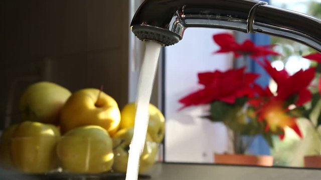 A person opening and closing the tap in the kitchen. There are fruits and vegetables around.