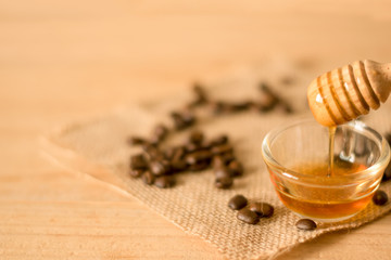 the Honey dipper and fragrant honey into a transparent bowl with coffee bean on wooden background. selective and soft focus at bowl