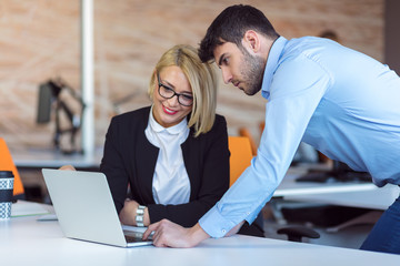 Colleagues chatting, sitting together at office table, smiling