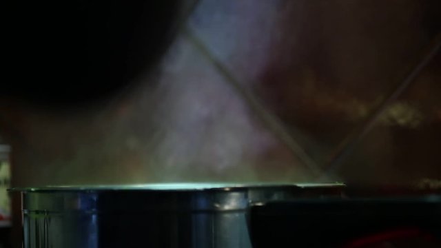 Hand with a slotted spoon is stirring the contents of a pot that is boiling. It is steam coming out of the pot.