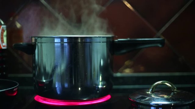 Water is boiling in a pot, on a kitchen hob. It is steam coming out of the pot.