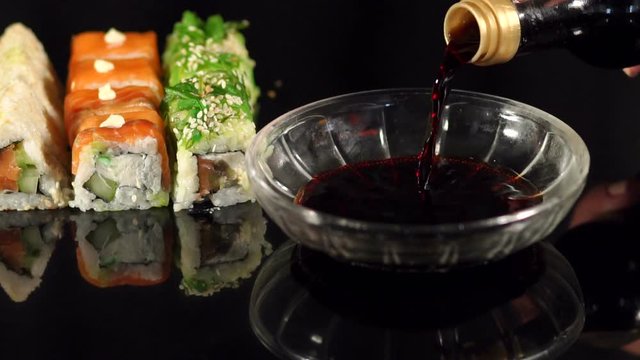 Japanese cuisine. Sushi. The girl pours soy sauce in a bowl on a black background.