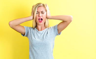 Young woman blocking her ears on a yellow background