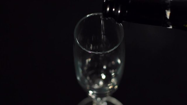 Champagne pouring into a glass on a black background close-up. Slow motion.