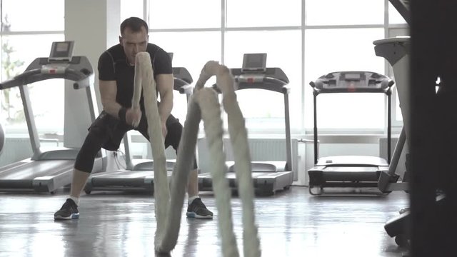 Slow motion of man with battle rope in functional training fitness gym