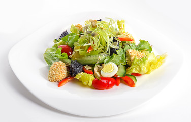 Fresh salad with tapenade, cucumbers, tomatoes and quail eggs on white dish. Isolated on white background. Front view.