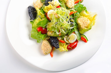 Fresh salad with tapenade, cucumbers, tomatoes and quail eggs on white dish. Isolated on white background. Top view.