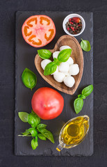 Mozzarella cheese, tomatoes and basil on a black stone table. Concept of Italian cuisine. Top view