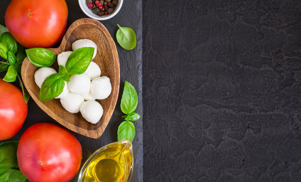 Mozzarella cheese, tomatoes and basil on a black stone table. Top view with copy space
