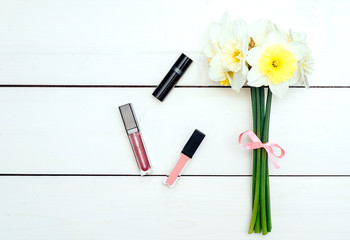 Top view on white wooden background with lip gloss and bouquet of narcissus. Liquid Lipstick