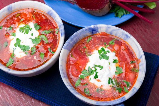 Ukrainian traditional borsch. Russian vegetarian red soup  in blue bowl on red wooden background.  Borscht, borshch with beet. Two plates. Top view.