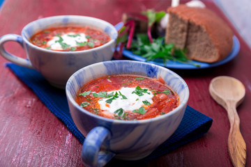 Ukrainian traditional borsch. Russian vegetarian red soup  in blue bowl on red wooden background.  Borscht, borshch with beet. Two plates. Close up.