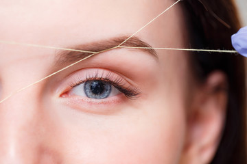 Cosmetologist plucks client eyebrows by thread