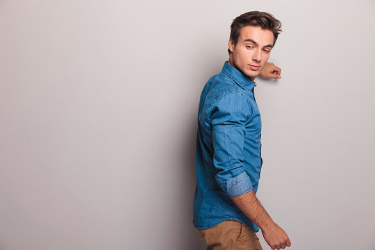 Man Leaning On Grey Wall Looks Back Over His Shoulder