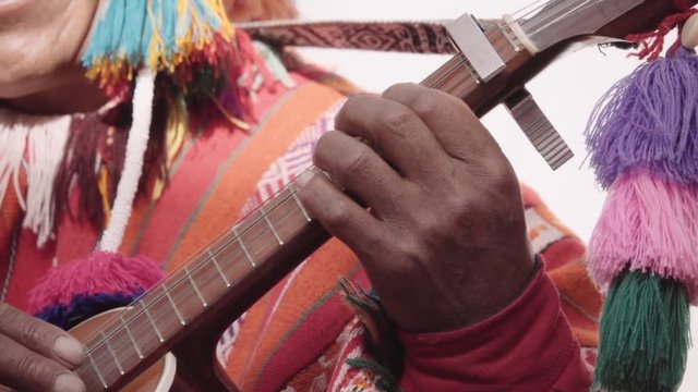 Detail of native quechua man using a colorful handcrafted chullo and a highlander hat, singing with his guitar on the alleys of Cusco	