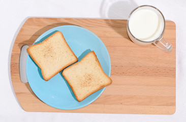 Square toast on a blue plate on a wooden board and a mug of milk