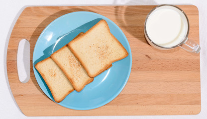 Square toast on a blue plate on a wooden board and a mug of milk