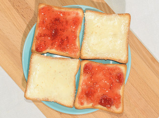 Square toast with jam on a blue plate on a wooden board and a mug of milk