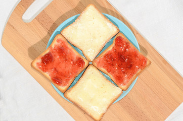 Square toast with jam on a blue plate on a wooden board and a mug of milk