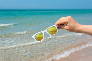 Sunglasses in hand on background of the beach