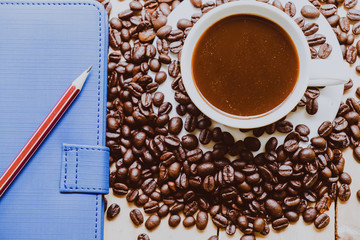 Cup of coffee white notebook, pencil, coffee beans on a Desktop from wooden plank. Top view.