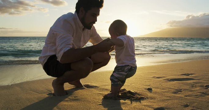 Young dad playing with baby son at the beach at sunset. Baby milestones first steps