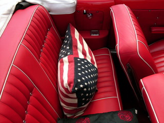 Kissen mit amerikanischer Flagge auf dem roten Rücksitz eines Cabriolet der Sechzigerjahre beim...