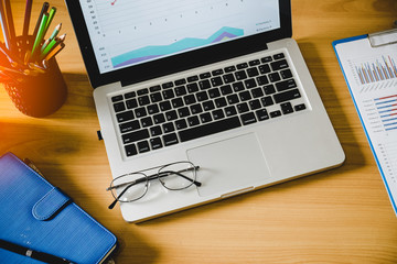 Eyeglasses on laptop keyboard and diary on wooden table