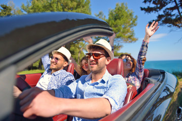 leisure, road trip, travel and people concept - happy friends driving in cabriolet car along...