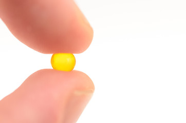 Contraceptive tablet without package, sandwiched two fingers against a light background.