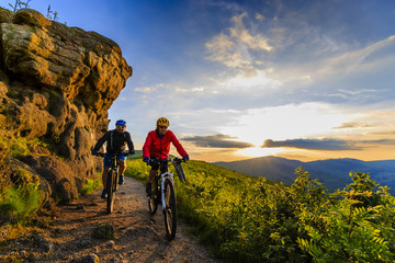 Obraz premium Mountain biking women and man riding on bikes at sunset mountains forest landscape. Couple cycling MTB enduro flow trail track. Outdoor sport activity.