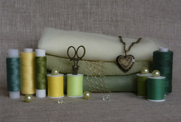 Coils with threads of green shades, fabric, sewing tools on a natural background