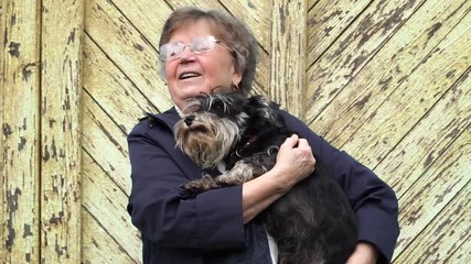 elderly 70 years caucasian woman with her miniature schnauzer dog pet on her hands, standing outdoor near the wooden wall
