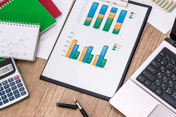 Financial graphs with laptop, calculator, pen on desk.