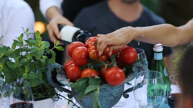 Woman takes cherry tomatoe from vase.