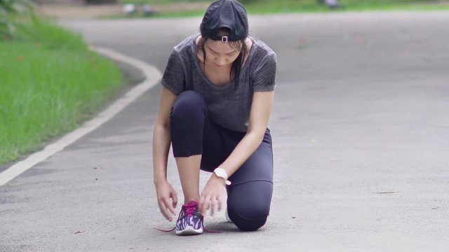 Running asian woman tying laces of running shoes before training