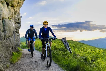Plexiglas foto achterwand Mountain biking women and man riding on bikes at sunset mountains forest landscape. Couple cycling MTB enduro flow trail track. Outdoor sport activity. © Gorilla