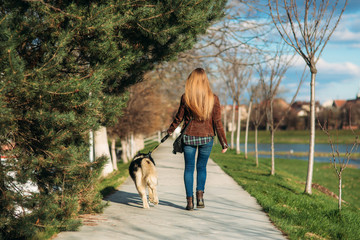 A girl is walking with a dog along the embankment. Beautiful Husky dog. The river. Spring.