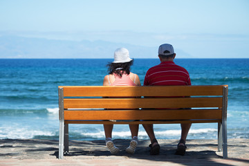 Seniors couple sitting on bench at the beach.Elderly couple looking to the sea
