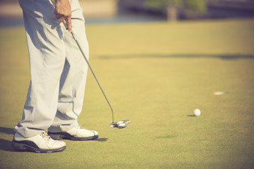 Golf player at the putting green hitting ball into a hole.vintage color