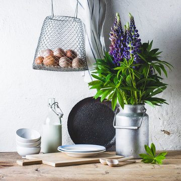 Concept of rural kitchen. Lupines in a can, milk, eggs and ware on a wooden table against the background of a white wall